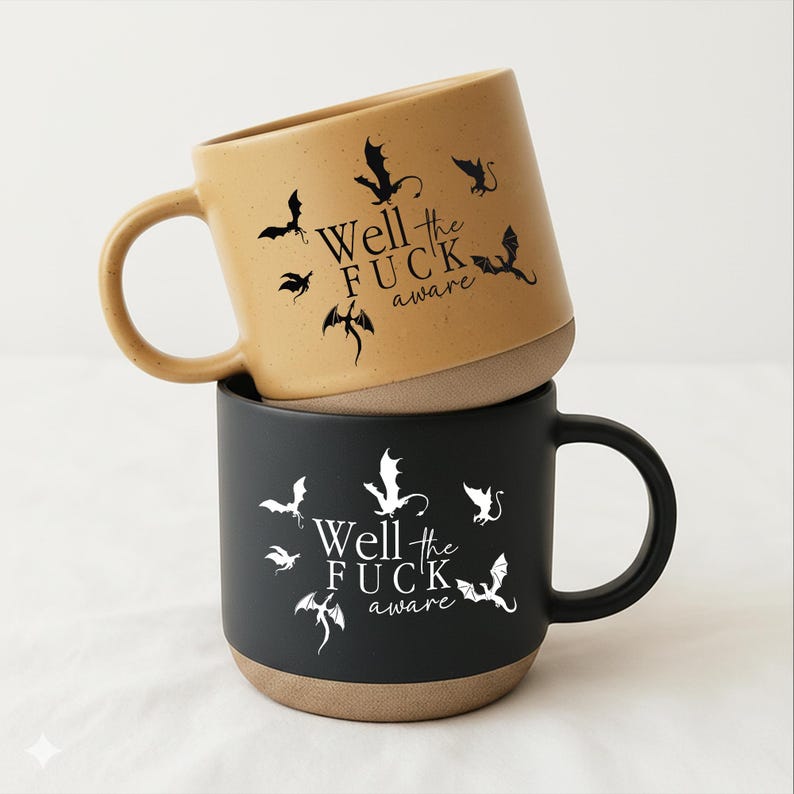 May include: Two ceramic mugs stacked on top of each other. The top mug is tan with black dragon silhouettes and the text "Well the FUCK aware." The bottom mug is black with white dragon silhouettes and the same text.