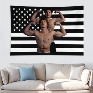 May include: A black and white tapestry featuring a stylized American flag design. The flag's stripes are black and white, with a field of white stars on a black background. Two muscular individuals are flexing their biceps in front of the flag.