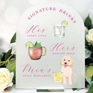 May include: A clear acrylic sign with an arched top, featuring the words "Signature Drinks" in pink script. Below, illustrations depict a vodka soda, Moscow Mule, and spicy margarita, with a dog illustration. The sign is displayed on a clear base.