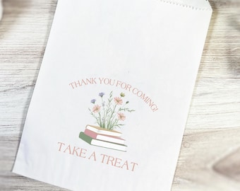 May include: White paper treat bag with a floral design and the text "THANK YOU FOR COMING! TAKE A TREAT". The design features a stack of books with flowers on top. The bag is on a light wood surface.