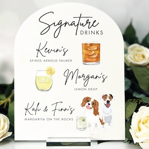 May include: White sign with a black arch at the top. The sign says "Signature Drinks" at the top. Below that are three drink options with names and descriptions. The first drink is "Kevin's" with the description "Spiked Arnold Palmer". The second drink is "Morgan's" with the description "Lemon Drop". The third drink is "Kali & Finn's" with the description "Margarita on the Rocks".