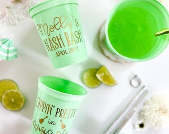 May include: Mint green plastic cups with gold lettering that reads "Molly's Nash Bash April 2019" and "Sippin' Pretty in Music City". The image also includes sunglasses, flowers, lime slices, and metal straws.