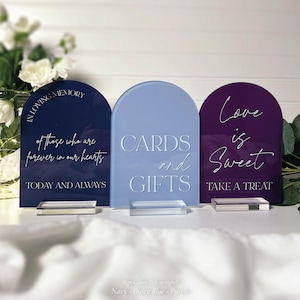 three rectangular signs with white text, placed on a white surface. The signs are blue, purple, and pink, and each has a different message written on it.