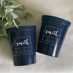 May include: Two navy blue stadium cups with white text. Each cup has the name "smith" in a square, with "HOLLYN AND TYLER" and the date "06.15.19" below. The hashtag "#HOLLYNTYSTHEKNOT" is at the bottom.