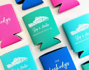 May include: A collection of colorful drink koozies in shades of blue, pink, and teal. Each koozie features white text and a graphic of a building. Some koozies have the text "Skip & Amelie, Wrightsville Beach, NC" and others say "The Laskodys".
