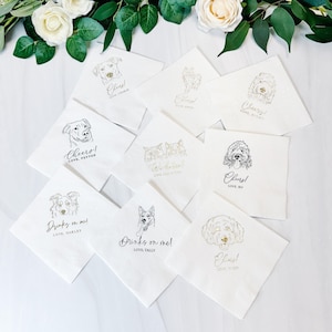 May include: A collection of white paper napkins with various dog illustrations in black and gold ink. Each napkin features a different dog breed, along with phrases like "Cheers!" and "Drinks on me!" and names. The napkins are arranged on a white surface.