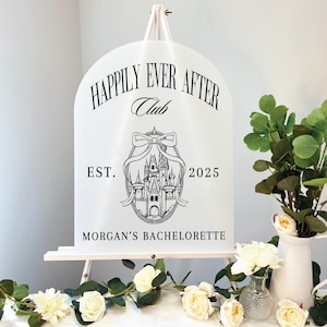 May include: White sign with black text and a black and white illustration of a castle. The sign reads "Happily Ever After Club Est. 2025 Morgan's Bachelorette"