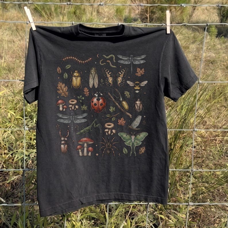 A vintage cottagecore print featuring a detailed collection of insects and woodland foliage. The layout centers on a large ladybug, surrounded by a centipede, dragonflies, a golden beetle, a cicada, a butterfly, a bumblebee, a praying mantis, a stag beetle, a spider, and a green luna moth. Interspersed among the detailed bugs are various red and brown mushrooms, autumn oak leaves, twigs, and tiny mystical stars. The artwork utilizes muted earthy tones for a classic nature aesthetic.