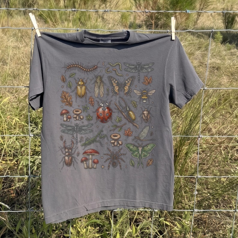 A vintage cottagecore print featuring a detailed collection of insects and woodland foliage. The layout centers on a large ladybug, surrounded by a centipede, dragonflies, a golden beetle, a cicada, a butterfly, a bumblebee, a praying mantis, a stag beetle, a spider, and a green luna moth. Interspersed among the detailed bugs are various red and brown mushrooms, autumn oak leaves, twigs, and tiny mystical stars. The artwork utilizes muted earthy tones for a classic nature aesthetic.