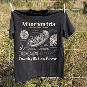 A cream-colored educational biology print titled "Mitochondria" and "POWERHOUSE OF THE CELL" in a bold serif font. The layout features detailed vintage engraving-style diagrams including a cross-section of a mitochondrion with labels like Cristae and Matrix, a cell diagram, a DNA strand, and an ATP molecular structure. Slogans read "we make ATP so you don't have to" and "Powering life Since Forever!" at the bottom. The entire design has a clean, high-contrast textbook aesthetic.
