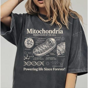 A cream-colored educational biology print titled "Mitochondria" and "POWERHOUSE OF THE CELL" in a bold serif font. The layout features detailed vintage engraving-style diagrams including a cross-section of a mitochondrion with labels like Cristae and Matrix, a cell diagram, a DNA strand, and an ATP molecular structure. Slogans read "we make ATP so you don't have to" and "Powering life Since Forever!" at the bottom. The entire design has a clean, high-contrast textbook aesthetic.