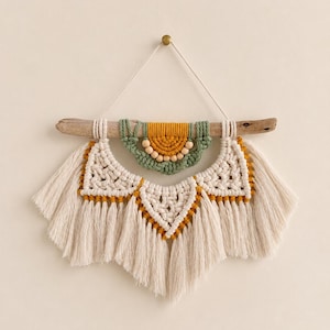 May include: A wall hanging featuring off-white macrame cord knotted into triangular patterns with long fringe. A smaller semi-circular section in mustard yellow and sage green sits above, accented with light wooden beads on a piece of driftwood.