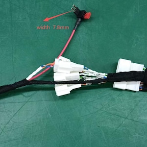 May include: Electrical wiring harness with multiple connectors and wires of various colours. The image shows a black connector, white connectors, and a red wire with a width of 7.8mm. The harness is on a green surface.