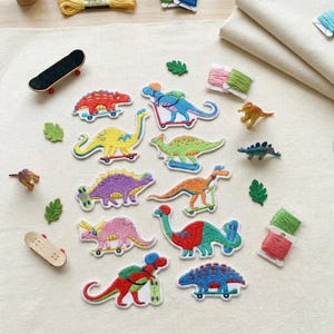 May include: A collection of embroidered dinosaur patches featuring various species riding skateboards and scooters, accompanied by two miniature toy skateboards, small green felt leaves, and several spools of colorful embroidery thread.