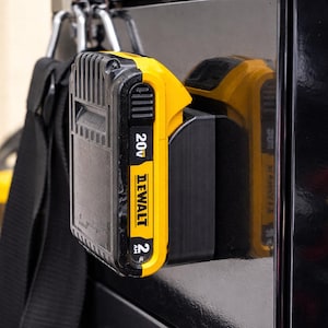 May include: A black and yellow DeWalt 20V 2Ah battery pack attached to a black surface. The battery is in a holder, and the DeWalt logo is visible. The image is a close-up of the battery and holder.