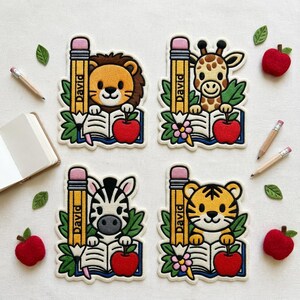 May include: Four embroidered patches featuring a lion, giraffe, zebra, and tiger, each holding a pencil labeled David and an open book with a red apple. The set includes scattered felt leaves, three wooden pencils, and three red felt apples.