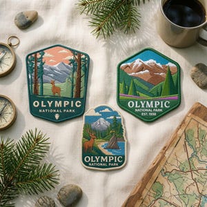 May include: Three embroidered patches featuring Olympic National Park landscapes. The left patch shows a deer in a forest, the top right shows snow-capped mountains, and the bottom center shows a deer by a lake. Each patch includes the text Olympic National Park.