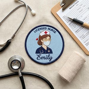 May include: A circular embroidered patch featuring a nurse with brown hair, glasses, and a white face mask with a red cross, wearing a dark blue uniform. The text reads LICENSED NURSE and Emily. The patch is surrounded by a stethoscope and clipboard.