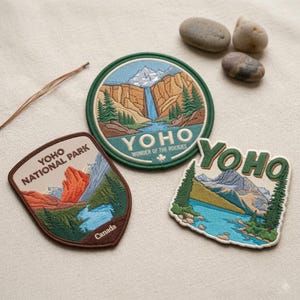 May include: Three embroidered patches featuring Yoho National Park. One circular patch shows a waterfall and mountains with the text YOHO WONDER OF THE ROCKIES. A shield-shaped patch reads YOHO NATIONAL PARK Canada. A third patch reads YOHO over mountains.