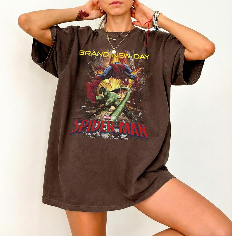 May include: A dark brown short-sleeve t-shirt featuring a graphic print of Spider-Man and the Hulk in a dynamic action scene. The text reads BRAND NEW DAY above the characters and SPIDER-MAN in large red letters at the bottom of the graphic.
