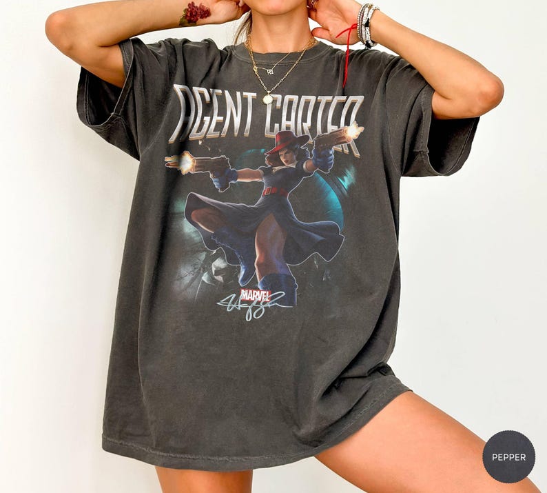 Pu&ograve; includere: T-shirt grigio scuro di Agent Carter con una grafica del personaggio che tiene due pistole. La maglietta ha la scritta "AGENT CARTER" e il logo Marvel. La maglietta ha una vestibilit&agrave; oversize e un aspetto vintage. L'immagine &egrave; stampata sul davanti.