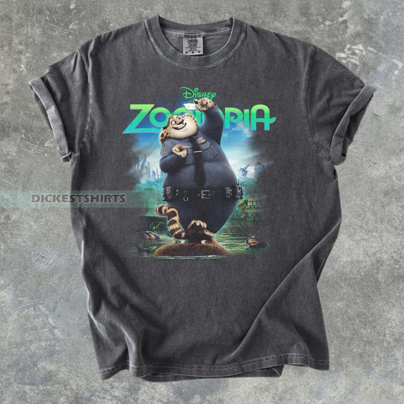 K&ouml;nnte beinhalten: Ein anthrazitfarbenes Kurzarm-T-Shirt mit einem Grafikdruck der Zootopia-Figur Officer Clawhauser. Die Figur tr&auml;gt eine blaue Polizeiuniform und h&auml;lt ein Telefon. Das Wort Zootopia ist in leuchtendem Gr&uuml;n dar&uuml;ber aufgedruckt.