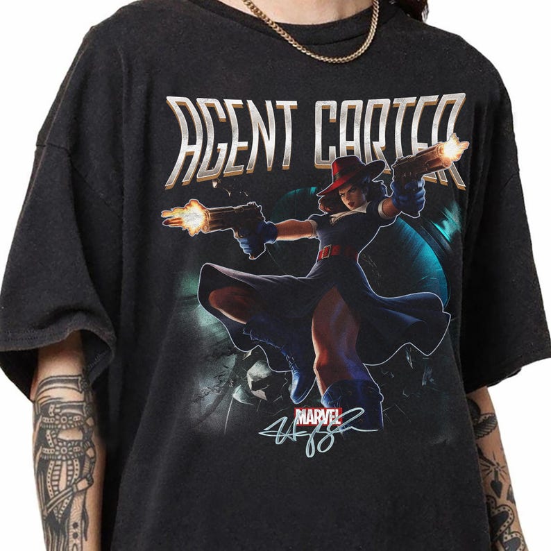 Pu&ograve; includere: T-shirt nera con grafica di Agent Carter della Marvel, che tiene due pistole con fiamme. Il testo "AGENT CARTER" &egrave; sopra il personaggio. Il logo Marvel e la firma sono in basso.