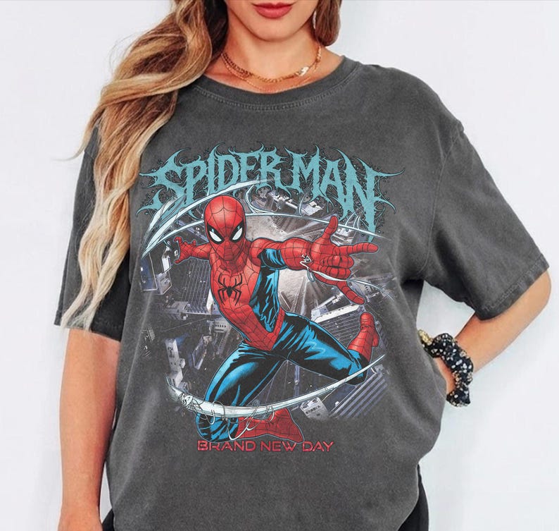 May include: Dark gray t-shirt featuring a graphic of Spider-Man in a dynamic pose, with the words "SPIDER MAN" in a stylized font. The phrase "BRAND NEW DAY" is printed below the image.