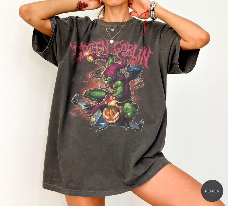 May include: Dark gray t-shirt featuring a Green Goblin graphic. The design includes the text "GREEN GOBLIN" in a distressed, pink font, and a detailed illustration of the Green Goblin character. The shirt has a vintage, worn look.