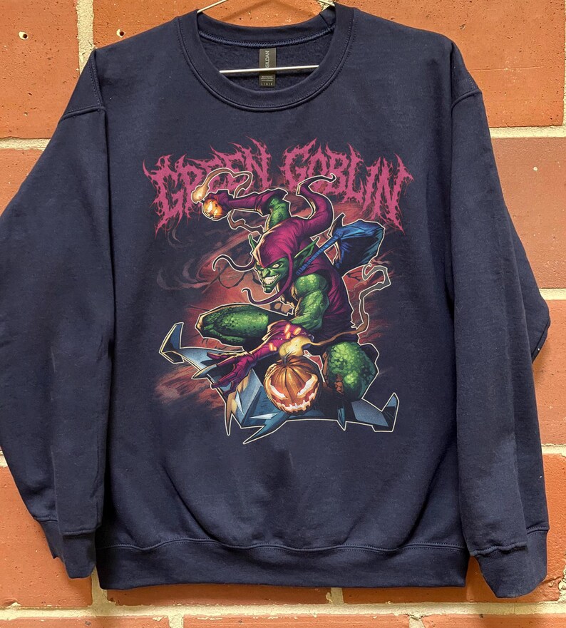 May include: Navy blue sweatshirt featuring a graphic of the Green Goblin character. The design includes the text "GREEN GOBLIN" in a stylized font, along with an illustration of the character in action. The sweatshirt is a crew neck style.