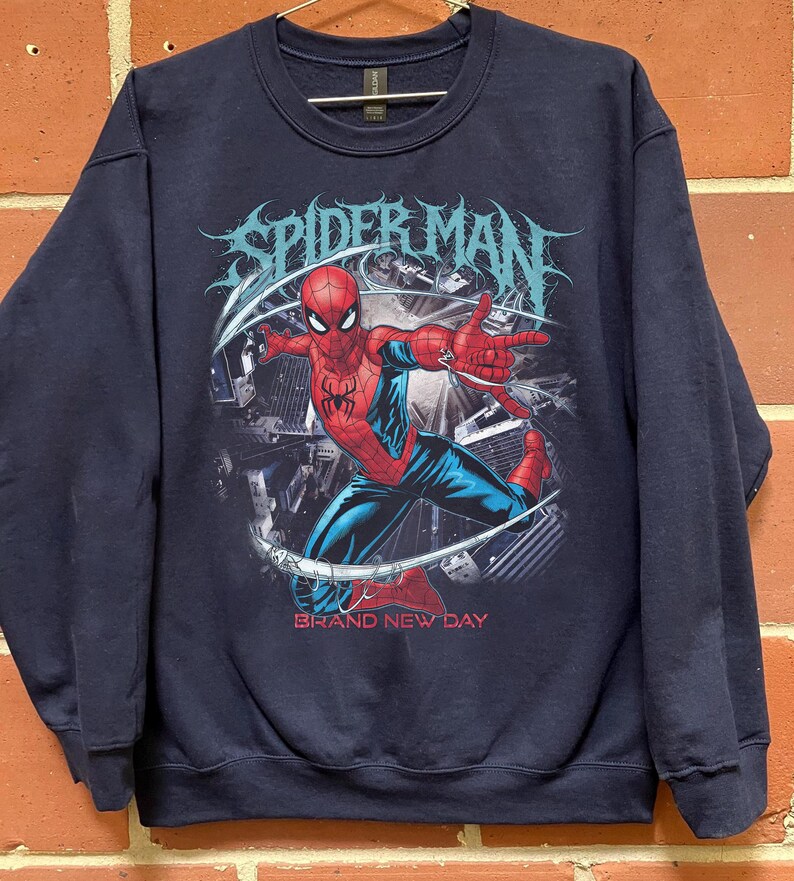 May include: Navy blue sweatshirt featuring a graphic of Spider-Man in a dynamic pose. The design includes the words "SPIDER MAN" in a stylized font and "BRAND NEW DAY" in red. The superhero is depicted in his classic red and blue suit.
