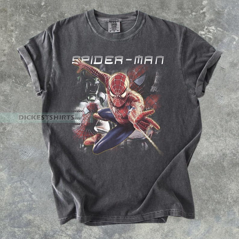 May include: A charcoal gray short-sleeve t-shirt featuring a graphic print of the character Spider-Man in a dynamic pose. The text SPIDER-MAN is printed in white above the character, and the text DICESTSHIRTS is visible on the left side.