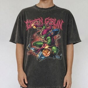 May include: Dark gray t-shirt featuring a Green Goblin graphic. The design includes the text "GREEN GOBLIN" in pink, and an illustration of the Green Goblin character. The shirt has a vintage, washed look.