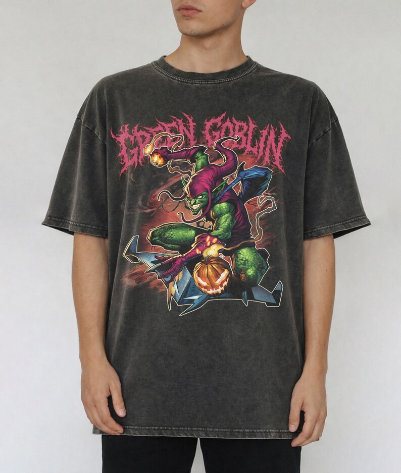 May include: Dark gray t-shirt featuring a Green Goblin graphic. The design includes the text "GREEN GOBLIN" in pink, and an illustration of the Green Goblin character. The shirt has a vintage, washed look.