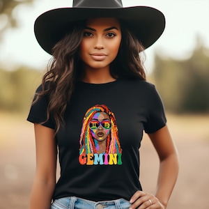 May include: A black short-sleeved t-shirt featuring a graphic print of a person with multicoloured braided hair wearing sunglasses with Gemini and Virgo zodiac symbols. The word Gemini is printed in large, colourful, bubble-style letters below.