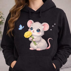 May include: A black hooded sweatshirt featuring a graphic print of a light gray mouse with large blue eyes holding a yellow dandelion flower. A small blue butterfly is positioned to the left of the mouse, and three tiny white flowers are on the right.
