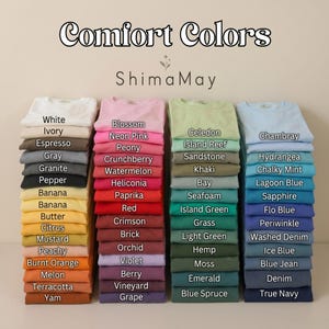 May include: A display of Comfort Colors t-shirts in a range of hues, such as pink, green, and blue. Each stack of shirts is labelled with its colour name. The brand name "Shima May" is also shown.