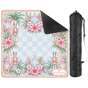 Puede incluir: Una manta de picnic decorativa con un patr&oacute;n de cuadros azul claro y blanco, con ilustraciones florales y de cascanueces. La manta tiene una parte inferior negra y viene con una bolsa de transporte negra. El texto "OAK & PALM CO." es visible.