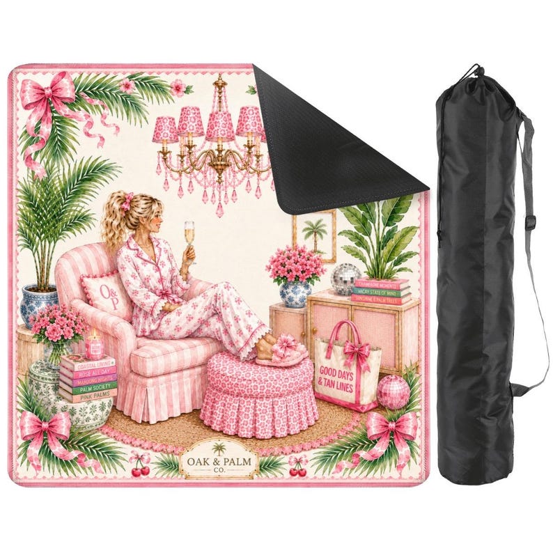 May include: A pink and white patterned beach blanket with a black underside, featuring a woman in pajamas, a pink armchair, and a chandelier. Includes a black carrying bag with a shoulder strap. The blanket has the text "GOOD DAYS & TAN LINES".