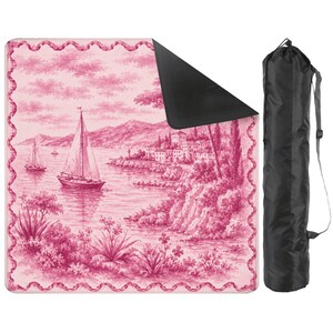 May include: A pink and white picnic blanket with a scenic illustration of sailboats on a lake, a village, and mountains. The blanket has a black underside and a decorative border. A black carrying bag is included.