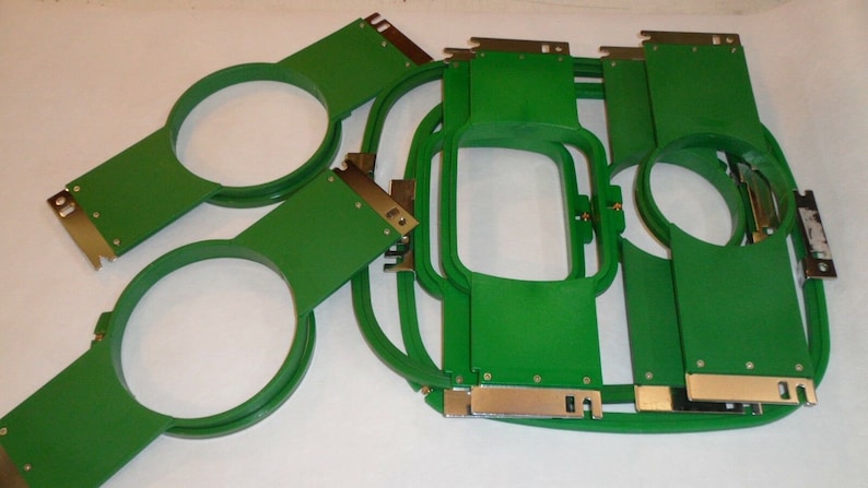 Puede incluir: Un conjunto de aros de bordado verdes con abrazaderas de metal plateado. Los aros son de varios tama&ntilde;os, incluyendo redondos y rectangulares.