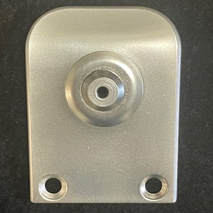 May include: A silver metal plate with a round, recessed area in the center. The plate has two holes on the bottom edge.