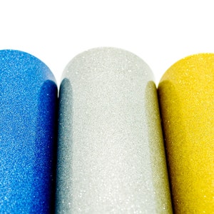 May include: Close-up of three cylindrical objects with a glittery finish. The cylinders are in blue, silver, and gold. The objects are set against a white background.