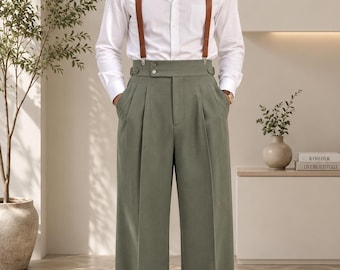 Könnte beinhalten: Ein weißes, langärmeliges Hemd mit Knopfleiste kombiniert mit einer hoch taillierten, weit geschnittenen Hose in Salbeigrün mit doppelten Falten und seitlichen Knopfriegeln. Das Outfit umfasst braune Lederhosenträger und passende Lederschuhe.