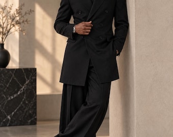 May include: A black double-breasted blazer with wide lapels, paired with matching black wide-leg trousers, a black button-down shirt, and a black tie. The ensemble is completed with black leather dress shoes and a silver wristwatch on the wrist.