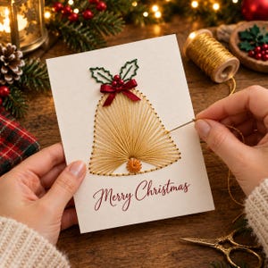 May include: A white greeting card featuring a hand-stitched gold thread bell design. The bell is topped with a small red ribbon bow, green embroidered leaves, and red beads. The text Merry Christmas is printed in red script at the bottom.