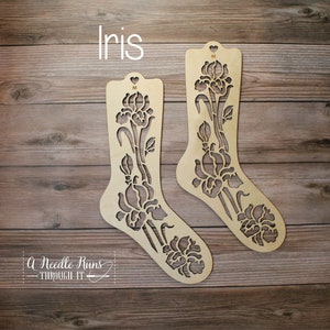 Puede incluir: Dos bloqueadores de calcetines de madera con un diseño de flor de iris. Los bloqueadores están etiquetados como "Iris".