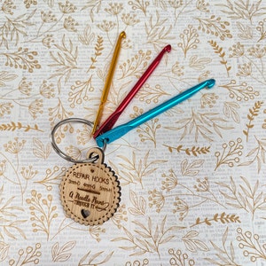 May include: A wooden keychain with a heart and the text "REPAIR HOOKS 3mm-D 4mm-G 5mm-H A Needle Runs Through It" attached to three crochet hooks in red, blue, and yellow.