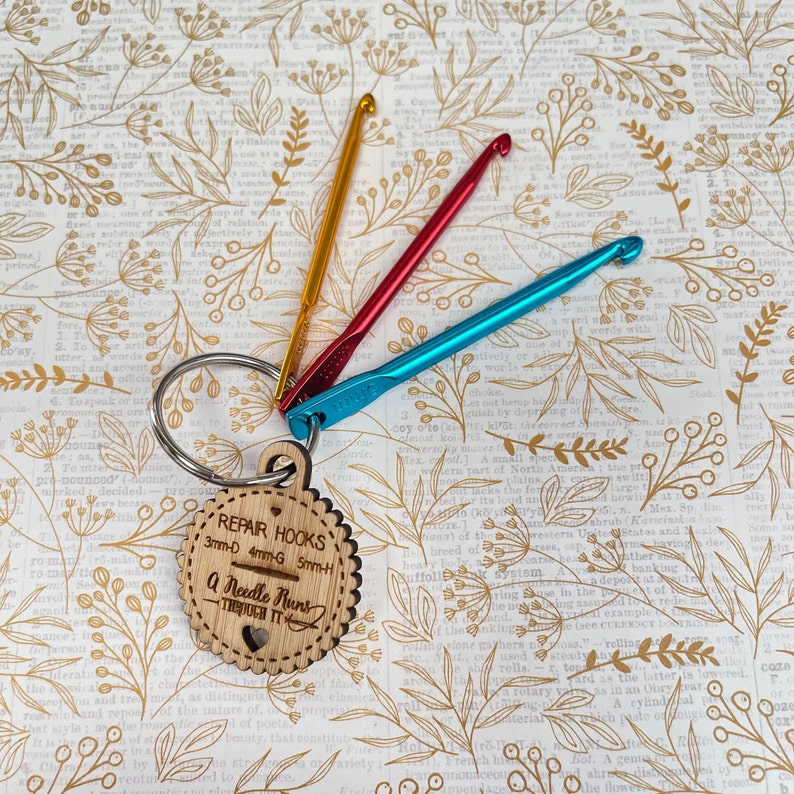 May include: A wooden keychain with a heart and the text "REPAIR HOOKS 3mm-D 4mm-G 5mm-H A Needle Runs Through It" attached to three crochet hooks in red, blue, and yellow.