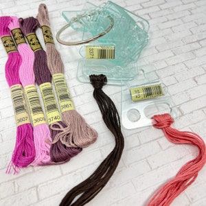 May include: Assortment of embroidery floss spools in pink, purple, brown, and beige colors. The spools are labeled with numbers 3607, 3609, 3740, and 3861. There are also two clear plastic organizers with numbers 3371 and 3712.